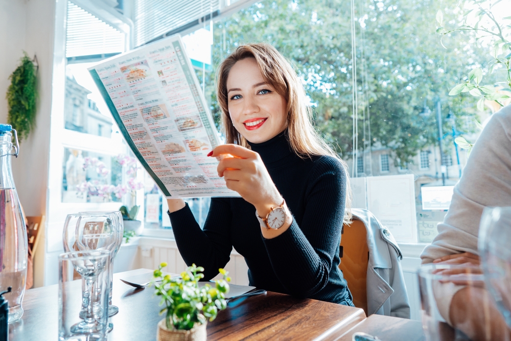 Mujer eligiendo platillo en menú impreso de restaurante - Megaprint imprime a toda la República Mexicana